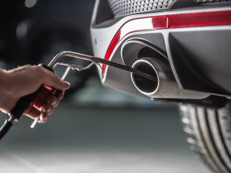 : Dieselskandal bei Hyundai & Kia: Männliche Hand, die eine Sonde in den Auspuff eines Fahrzeugs hält, um die Abgasemission zu messen.