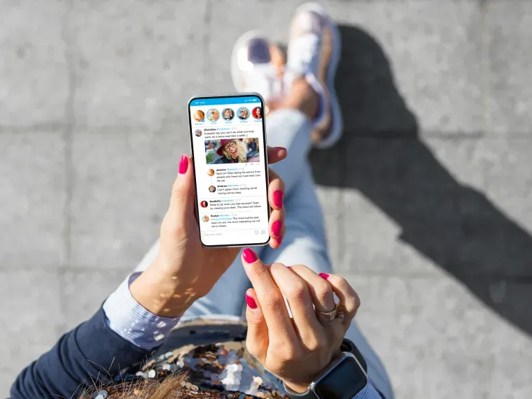 Frau hält ein Handy in der Hand auf dem Display ist ein Social Media Kanal zu sehen