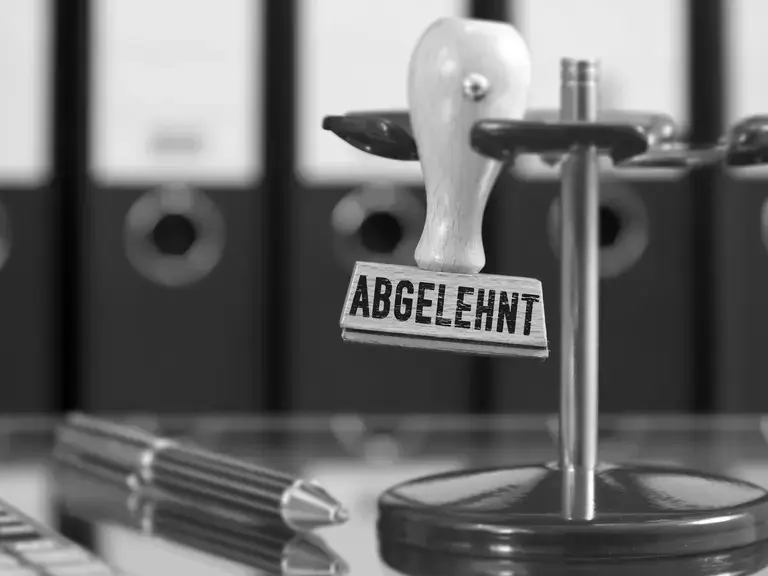 Ein Stempel mit der Aufschrift abgelehnt in einem Stempelhalter, daneben ein Stift
