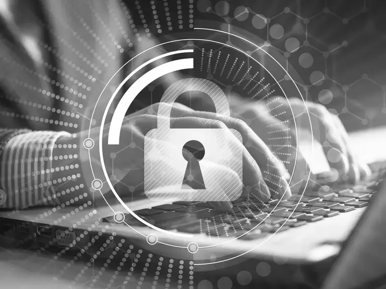 Hände, die auf einer Laptop Tastatur tippen. Im Vordergrund ist ein digitales Schloss eingeblendet