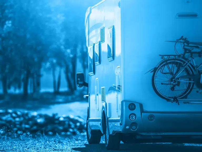 Heckansicht eines Wohnmobils, das über eine Waldstraße fährt.