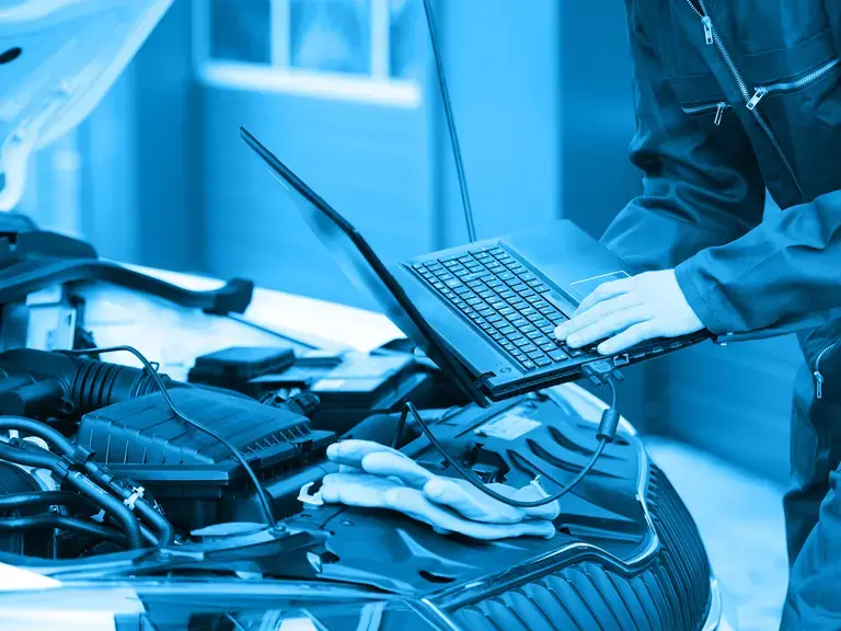 Ein Laptop an eine offene Motorhaube angeschlossen, das von einem Techniker gehalten wird