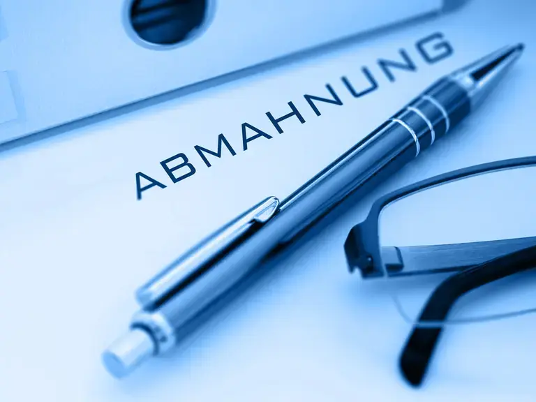 Ein Blatt auf dem Abmahnung steht, darauf liegen ein Stift und eine Brille
