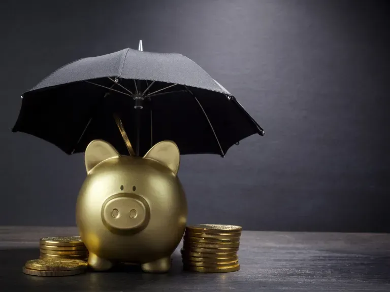 Ein goldenes Sparschwein mit Münzen daneben, das unter einem Schirm steht