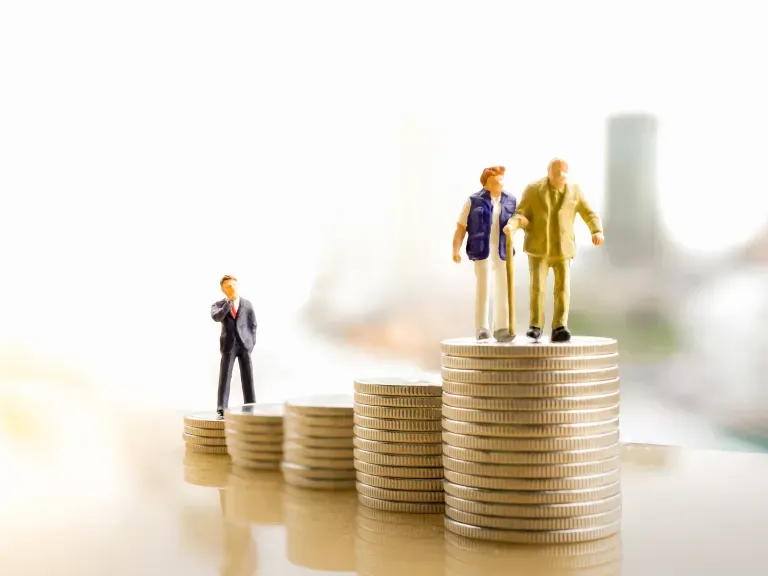Mehrere Stapel Münzen auf dem Vorderen stehen zwei Figuren, die ein Rentnerpaar darstellen