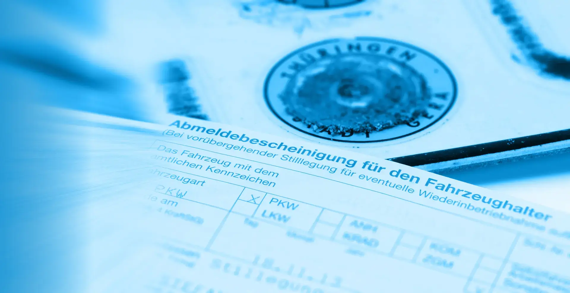 Ein Ausschnitt auf dem im Vordergrund ein Fahrzeugschein und im Hintergrund ein entwertetes Nummernschild zu sehen sind.