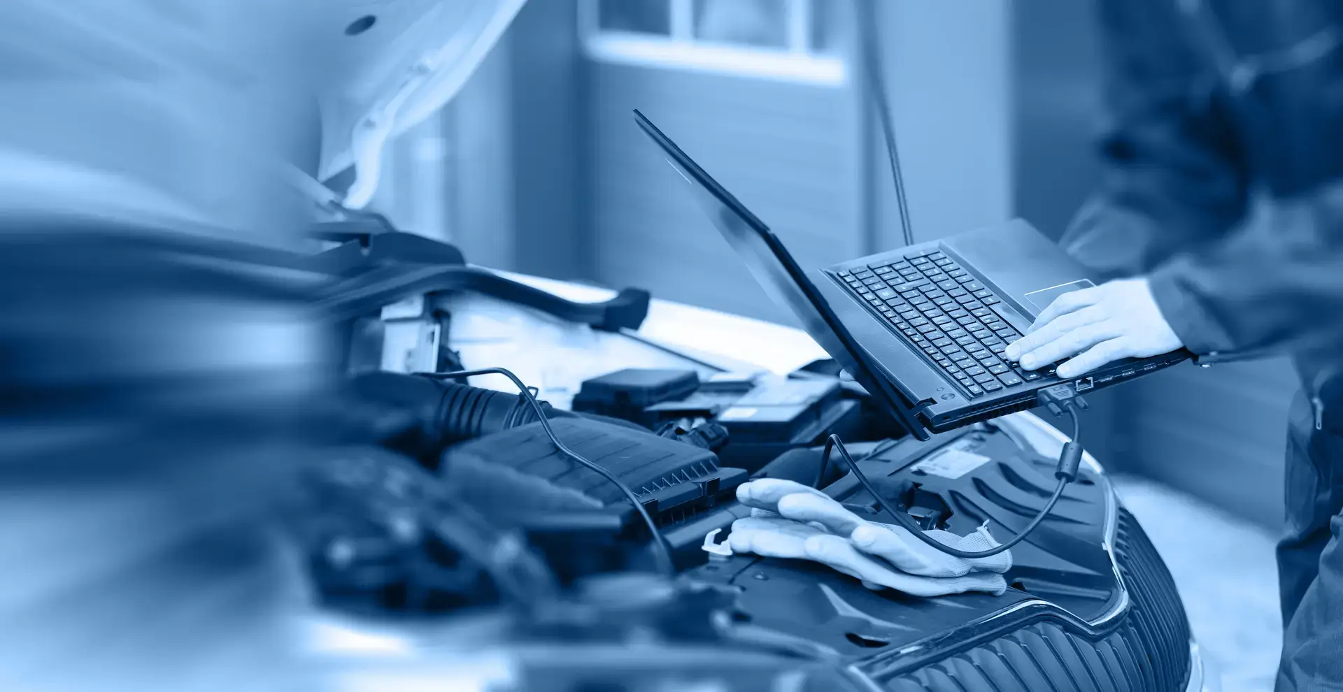 Eine geöffnete Motorhaub an die ein Laptop angeschlossen ist und von einem Techniker gehalten wird