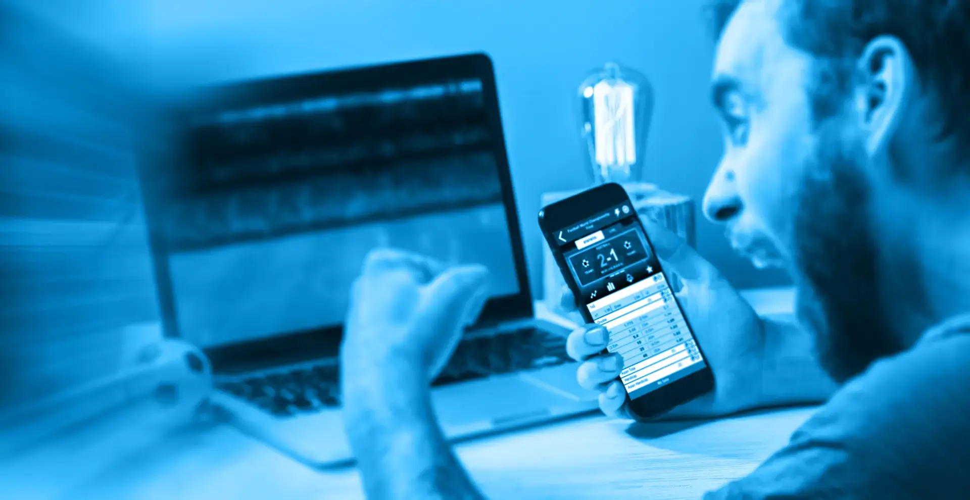 Ein Mann, der vor einem Laptop sitzt, ein Handy in der Hand hält und die Faust ballt.