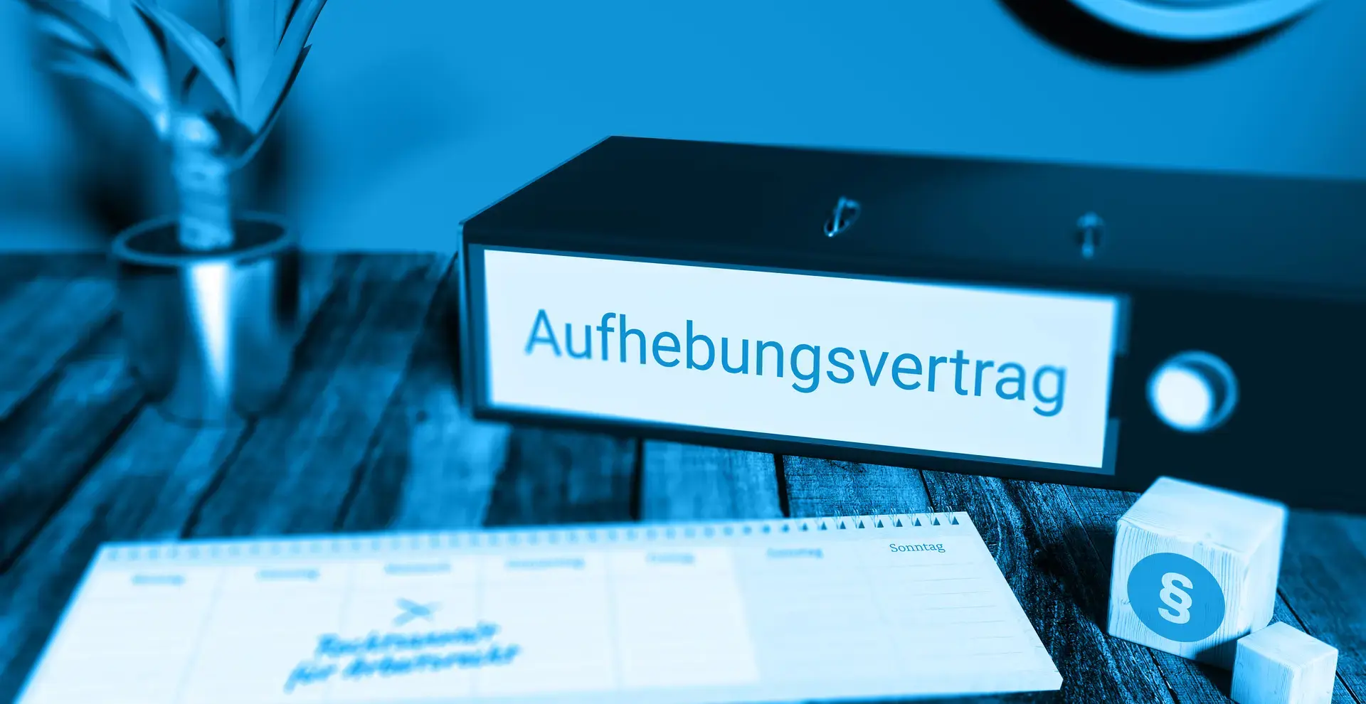 Ein Schreibtisch auf dem ein Ordner mit der Aufschrift Aufhebungsvertrag und ein Kalender liegen