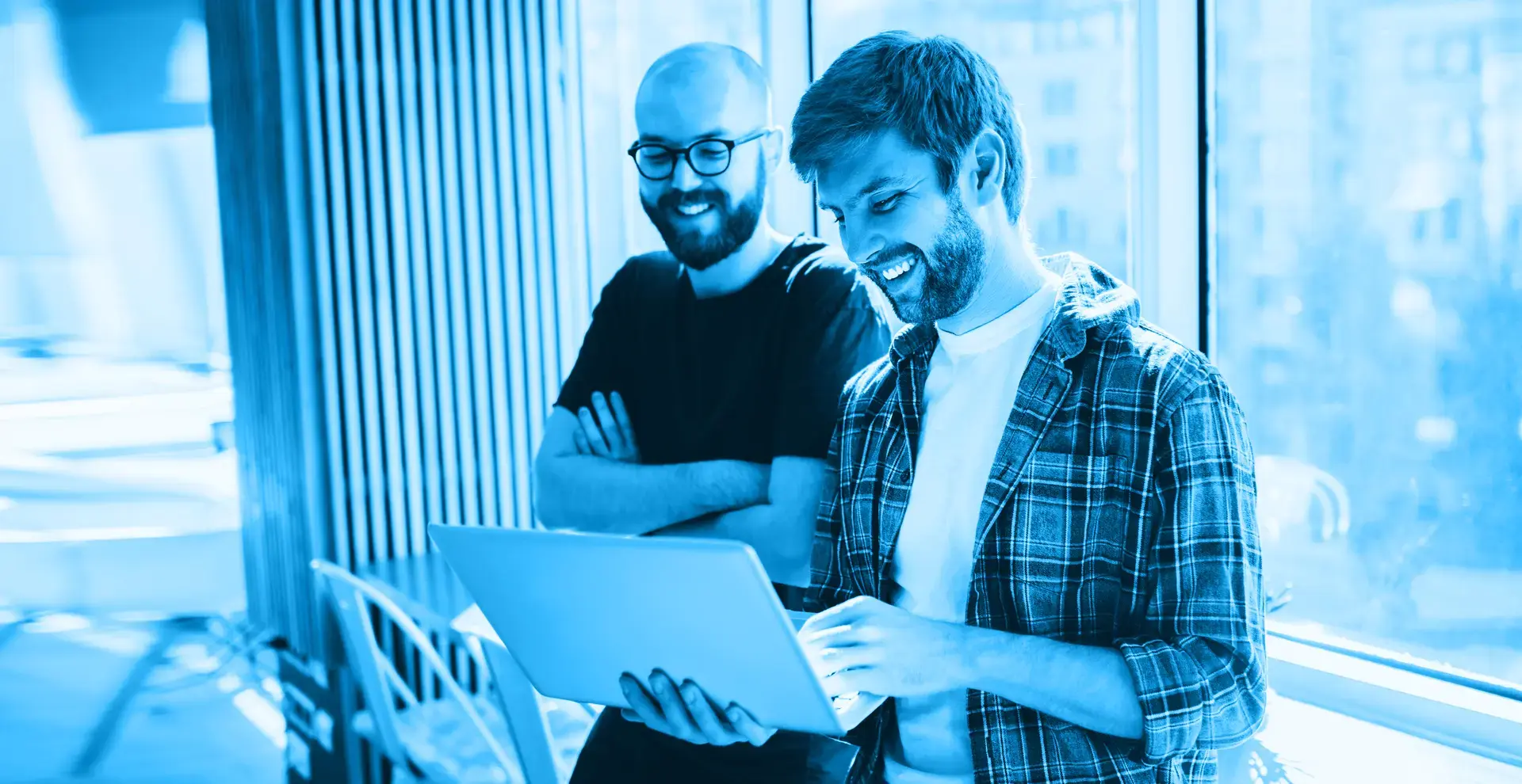 Zwei Männer, die sich an einem Schreibtisch anlehnen und auf ein Laptop schauen