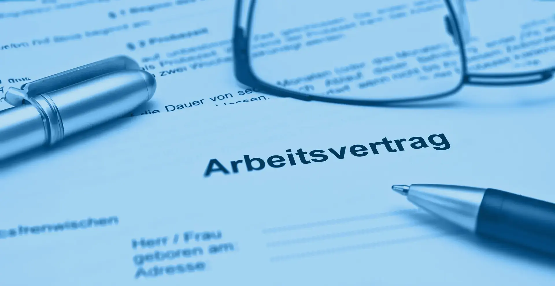 Teilausschnitt eines Arbeitsvertrag auf dem 2 Stifte und eine Brille liegen