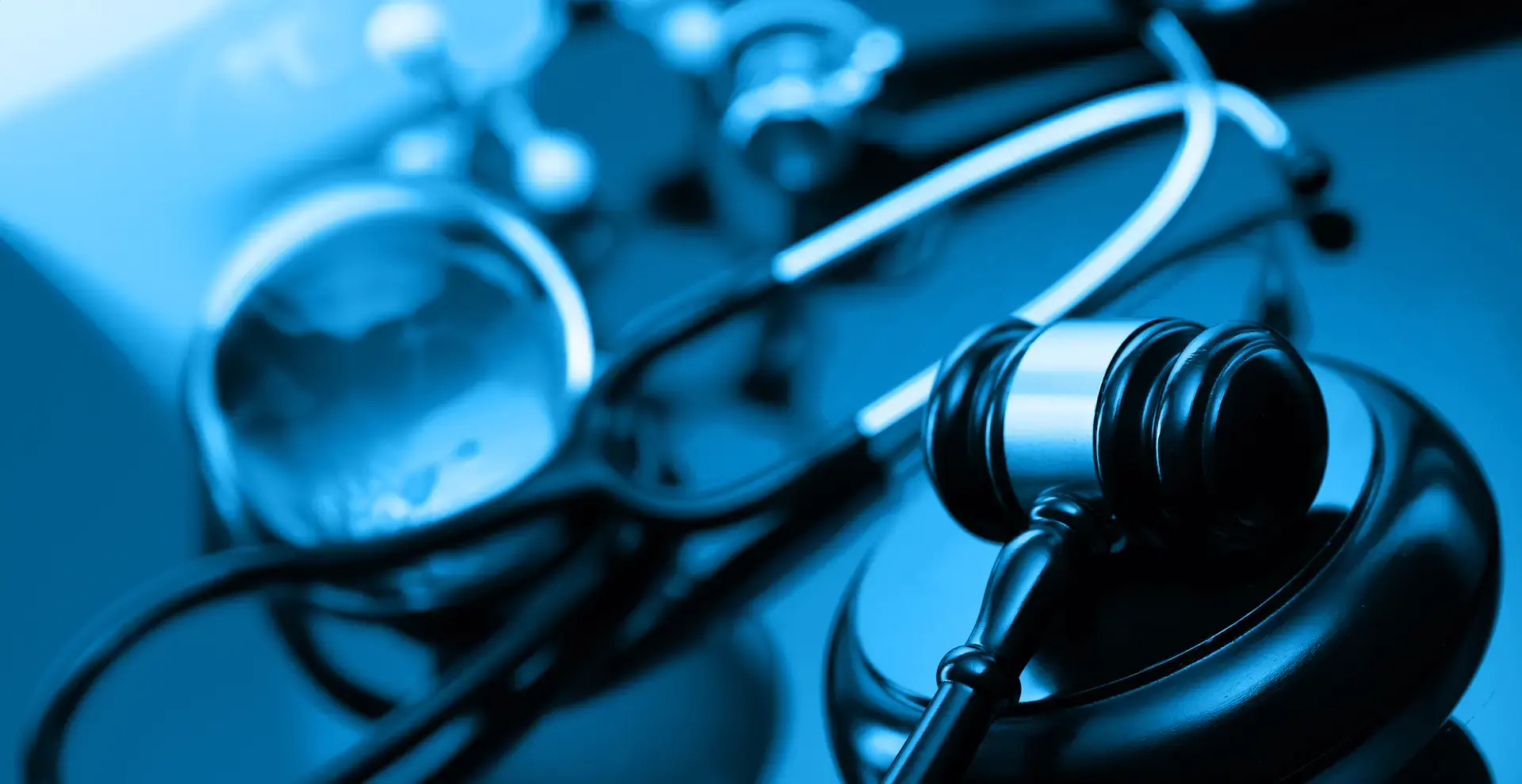 im Vordergrund ein Richterhammer, im Hintergrund ein Stethoskop und andere Arztutensilien