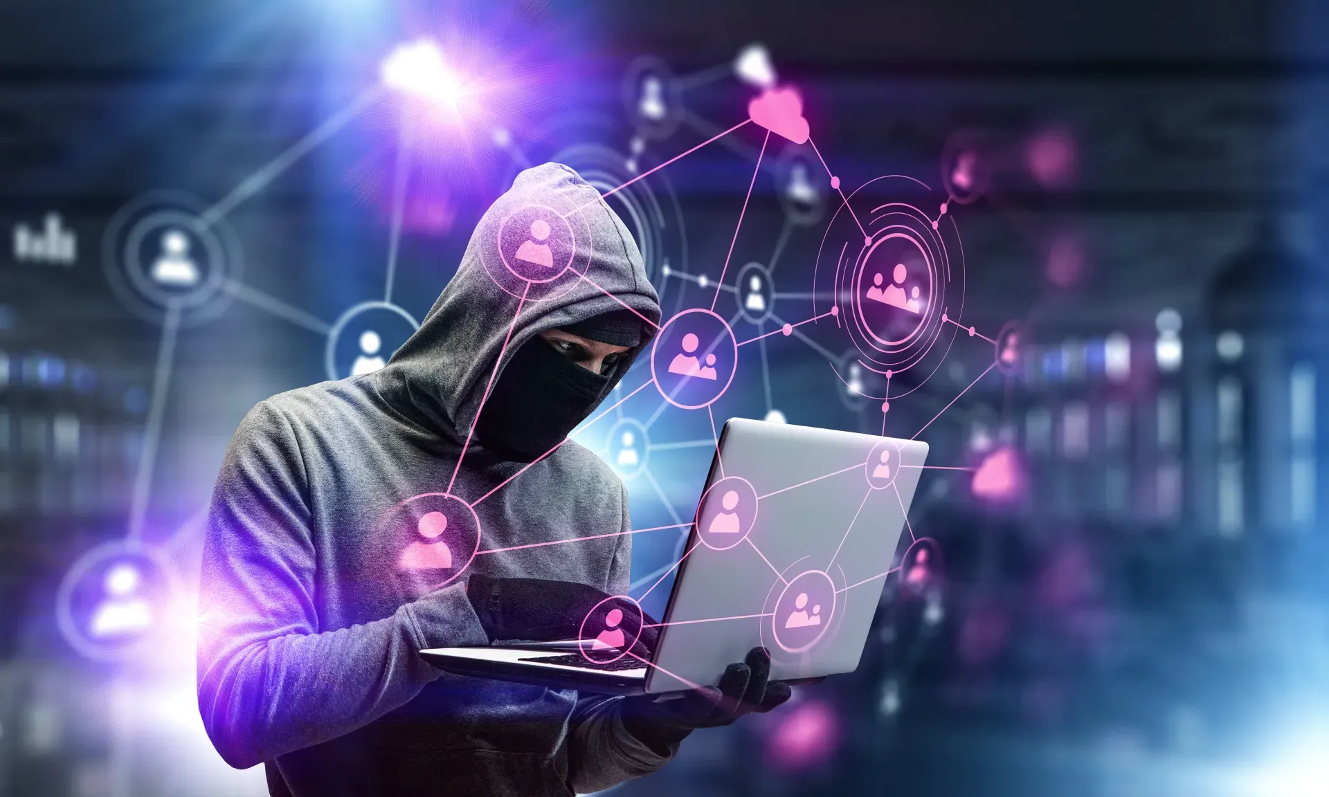 Ein vermummter Hacker mit Kapuze und Maske mit einem Laptop in der Hand