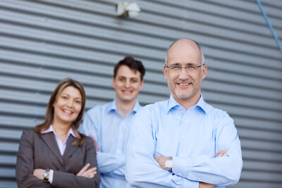 Vater, Mutter und Sohn posieren für ihr Familienunternehmen vor einer grauen Wand.