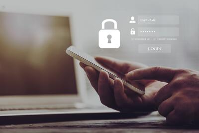 Ein Handy, das von seinem Nutzer bedient wird. Darüber ein Datenschutzsymbol in Form eines Schlosses