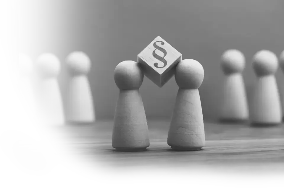 Spielfiguren zwischen die ein Würfel mit einem § aufgedruckt geklemmt ist.