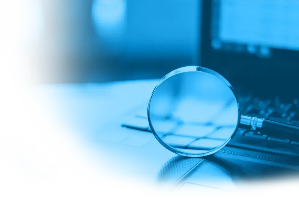Im Vordergrund eine Lupe, im Hintergrund ein Teil eines Laptops