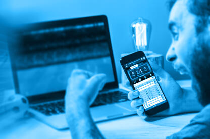 Ein Mann, der vor einem Laptop sitzt, ein Handy in der Hand hält und die Faust ballt.