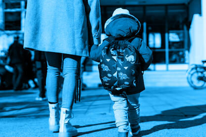 ein Mutter, die ihr Kind an der Hand hält und auf ein Gebäude zu geht