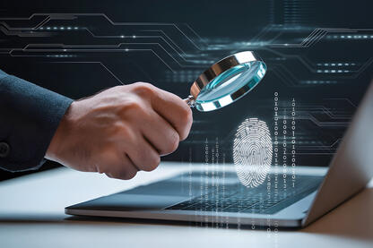 Lupe die über ein Laptop gehalten wird, aus dem ein Fingerabdruck und Zahlen nach oben schweben